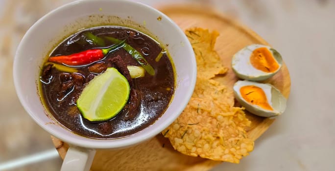 Rawon or Indonesian black beef soup, black color are from indonesian nut called kluwek. Served with lime, chili paste, salted egg, and tempe cracker. Perfect for recipe, article, or any cooking contents or blog