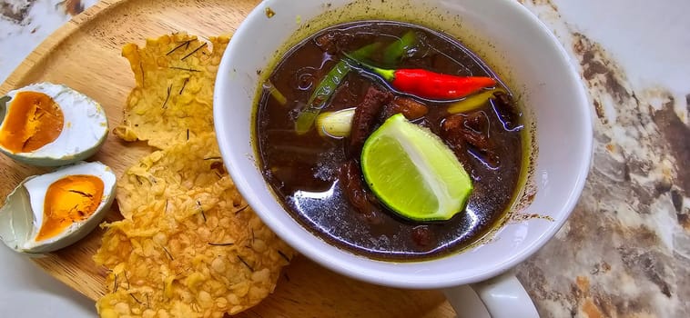 Rawon or Indonesian black beef soup, black color are from indonesian nut called kluwek. Served with lime, chili paste, salted egg, and tempe cracker. Perfect for recipe, article, or any cooking contents or blog