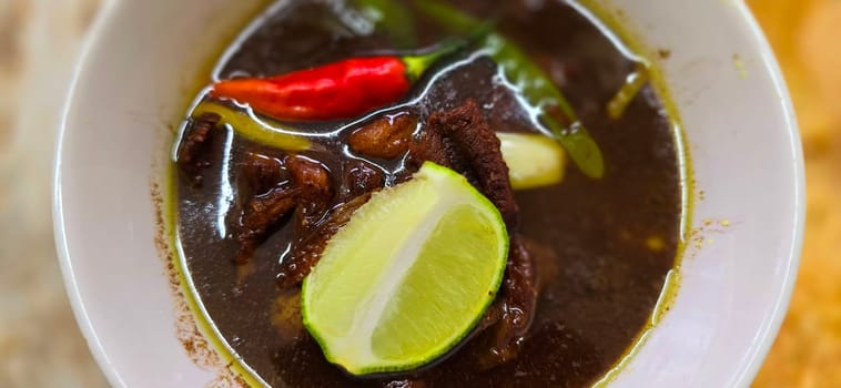 Rawon or Indonesian black beef soup, black color are from indonesian nut called kluwek. Served with lime, chili paste, salted egg, and tempe cracker. Perfect for recipe, article, or any cooking contents or blog