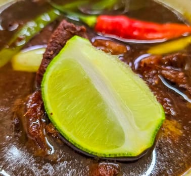 Rawon or Indonesian black beef soup, black color are from indonesian nut called kluwek. Served with lime, chili paste, salted egg, and tempe cracker. Perfect for recipe, article, or any cooking contents or blog