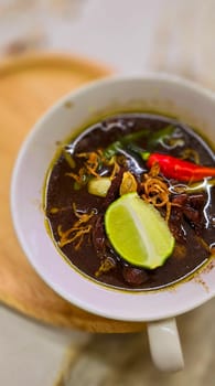 Rawon or Indonesian black beef soup, black color are from indonesian nut called kluwek. Served with lime, chili paste, salted egg, and tempe cracker. Perfect for recipe, article, or any cooking contents or blog