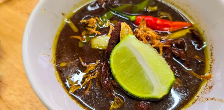 Rawon or Indonesian black beef soup, black color are from indonesian nut called kluwek. Served with lime, chili paste, salted egg, and tempe cracker. Perfect for recipe, article, or any cooking contents or blog