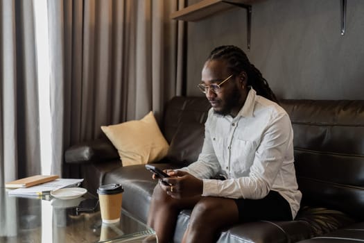 Young African American man relaxing on soft at home, texting messaging on smartphone. man using mobile phone chatting online message, shopping online from home.