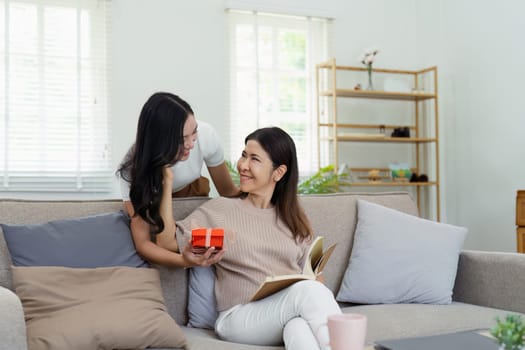 Congratulations. Loving asian mature daughter surprised mother with present in Mother's Day, giving her handmade card and gift box.