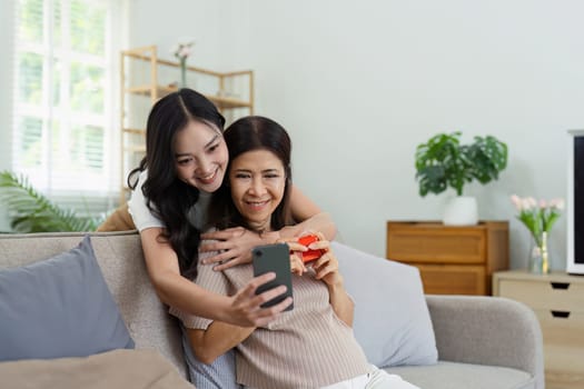 Congratulations. Loving asian mature daughter surprised mother with present in Mother's Day, giving her handmade card and gift box.