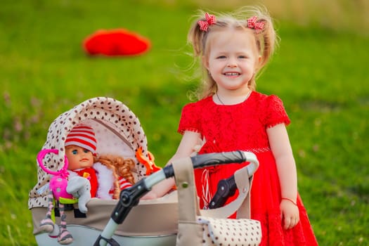 little girl plays with a doll and a stroller on the lawn