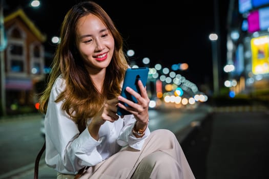 Asian woman on a night walk through the city streets multitasks with technology by using a laptop computer and mobile phone while talking.