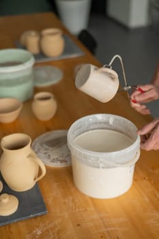 Close-up of a potter's hands glazing a ceramic mug. Vertical photo