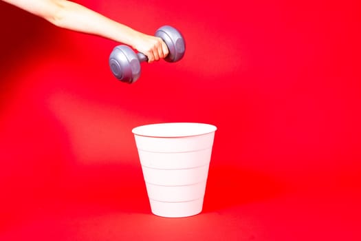 Dumbbells are thrown in the trash can. For copy space for designers on red background