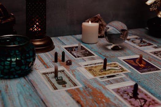 A dimly lit scene showing a spread of tarot cards, alongside crystals, candles, and a crystal ball on a rustic wooden table