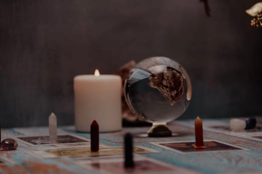 A dimly lit scene showing a spread of tarot cards, alongside crystals, candles, and a crystal ball on a rustic wooden table