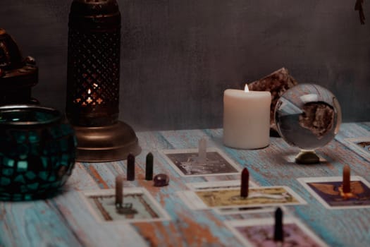 A dimly lit scene showing a spread of tarot cards, alongside crystals, candles, and a crystal ball on a rustic wooden table