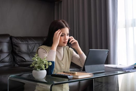 A middle-aged woman is tired while working from home in her bedroom with her laptop and pile of documents next to her..