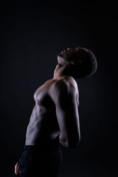 Athletic african american man topless, big muscles, a dark background studio