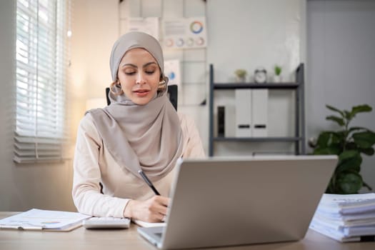 Muslim businesswoman working using laptop and taking notes on documents In the modern office.