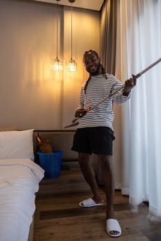 Playful African man in casual clothes Clean the dust or dirtiness of the room happily and have fun cleaning..