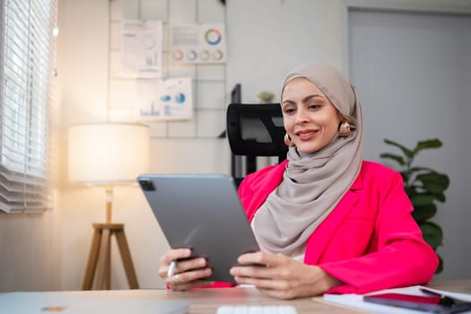 A female Muslim investor who trades in cryptocurrencies sits looking at stock charts and studying Bitcoin..