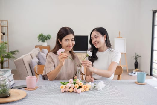 Middle-aged daughter happily arranges flowers with her mother at home Free time activities that are done together as a family.