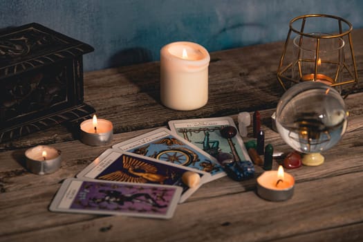 Close-up of a tarot card arrangement with a crystal ball and flickering candles on an aged wooden surface