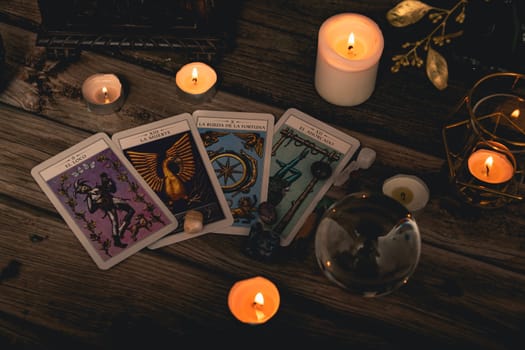 Close-up of a tarot card arrangement with a crystal ball and flickering candles on an aged wooden surface