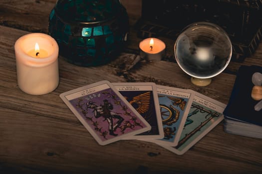 Close-up of a tarot card arrangement with a crystal ball and flickering candles on an aged wooden surface