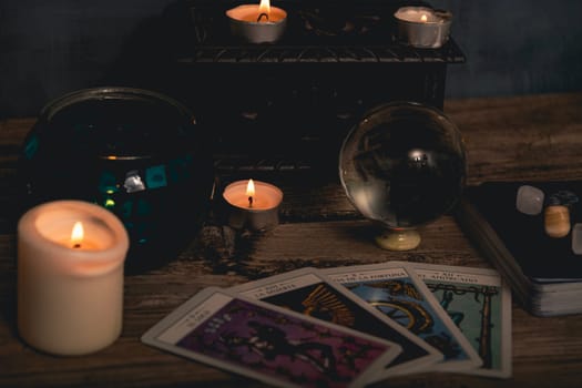 Close-up of a tarot card arrangement with a crystal ball and flickering candles on an aged wooden surface