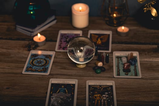 Close-up of a tarot card arrangement with a crystal ball and flickering candles on an aged wooden surface