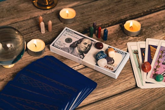 A tarot spread with The Fool card, hundred-dollar bills, and various crystals on a rustic wooden background with candles