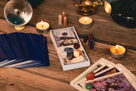 A tarot spread with The Fool card, hundred-dollar bills, and various crystals on a rustic wooden background with candles