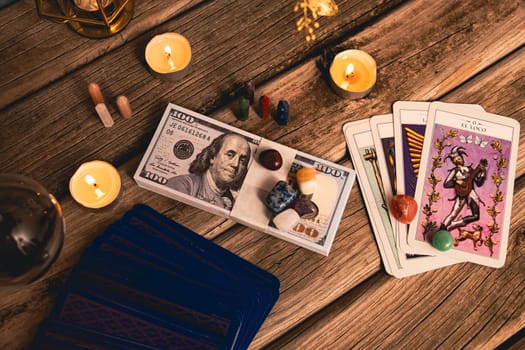 A tarot spread with The Fool card, hundred-dollar bills, and various crystals on a rustic wooden background with candles