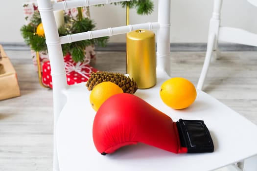 Sports equipment: dumbbell, boxing gloves, fir branch, Christmas ornament, gifts on a chair.