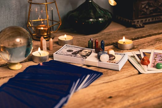 A tarot spread with The Fool card, hundred-dollar bills, and various crystals on a rustic wooden background with candles