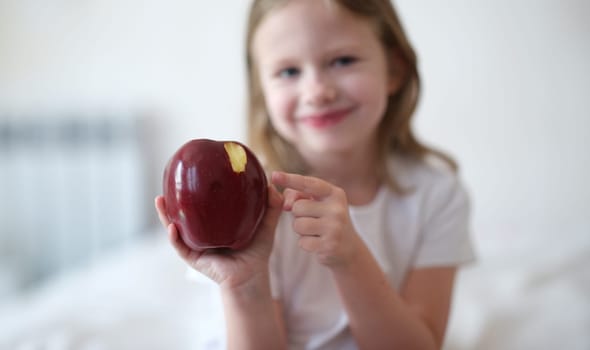 Beautiful little smiling girl eats red ripe apple. Benefits of apples for body concept
