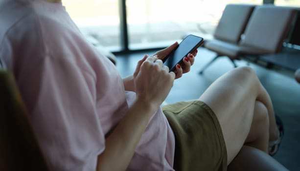 Woman traveler with smartphone in her hands sits in departure area at airport or train station. Application for gadgets of tourists or search for information for travelers concept