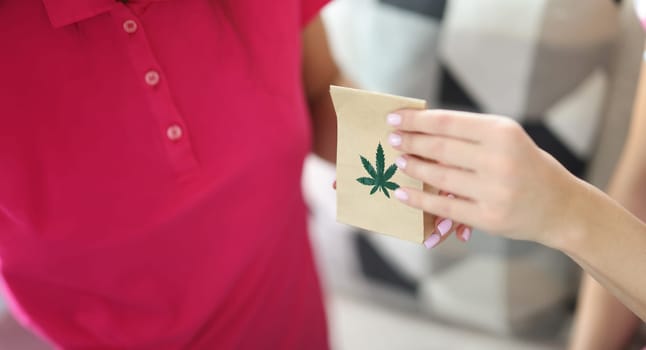 Woman hand passes paper bag with and marijuana closeup. Online delivery of marijuana products concept