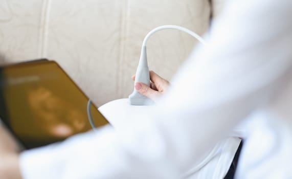 Doctor with ultrasound equipment during ultrasound medical examination of abdomen. Examination of fetus during pregnancy at home