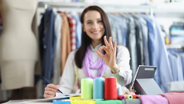 Dressmaker woman holding ok gesture while working in studio. Recommendations for tailoring stylish fashionable clothes and a successful atelier