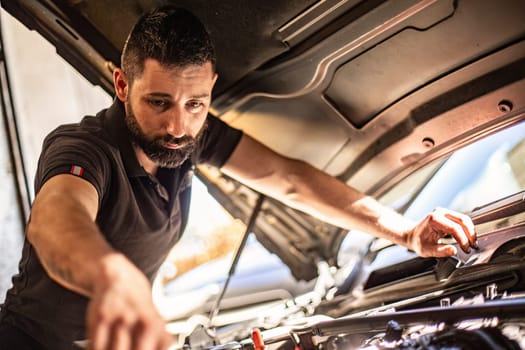 Milan, Italy 9 April 2024: Mechanic's hands delve into car engine under the hood, symbolizing repair and maintenance.