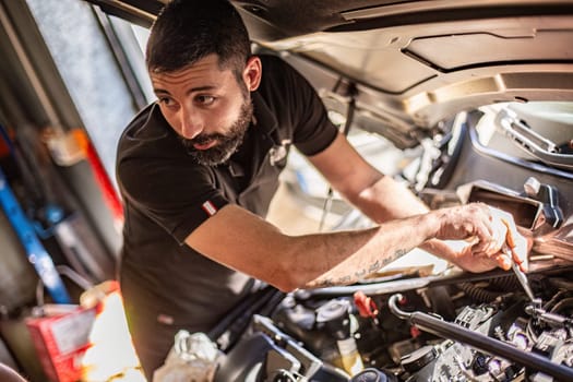 Milan, Italy 9 April 2024: Mechanic's hands delve into car engine under the hood, symbolizing repair and maintenance.