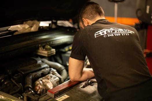 Milan, Italy 9 April 2024: Mechanic's hands delve into car engine under the hood, symbolizing repair and maintenance.