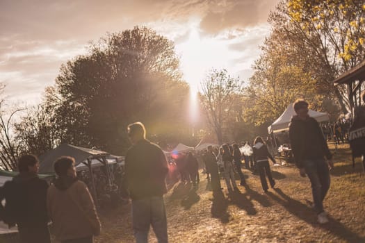 Milan, Italy 1 April 2024: A vibrant sunset rave party in a park, showcasing energetic silhouettes dancing.