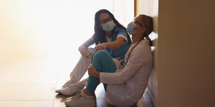 Surgeon in hospital corridor with communicates with doctor sitting on floor. High mortality and coronavirus pandemic. Medical error and death