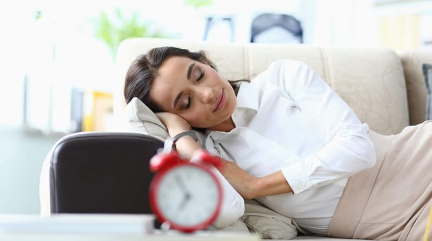 Young woman sleeps on sofa next to alarm clock. fatigue and drowsiness causes in women concept
