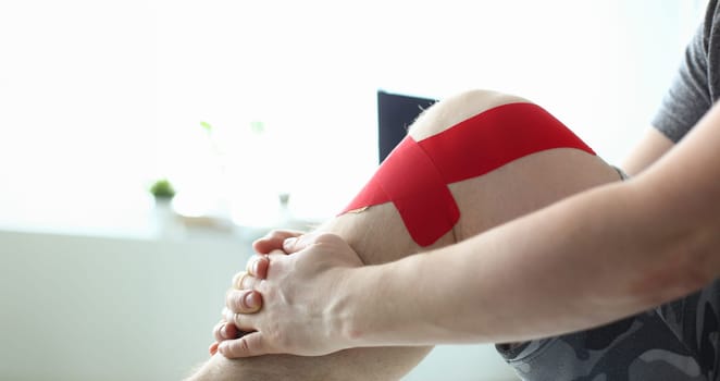 Therapeutic treatment of leg with red physio tape. Stretching knee joint concept