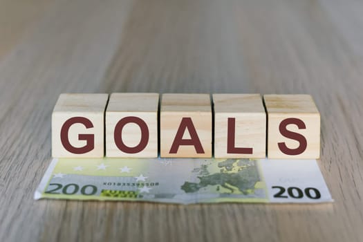 Goals word on a wooden cubes blocks, money 200 Euro banknotes. Management big salary career concept.