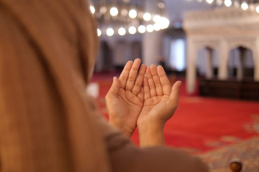 Muslim young woman in hijab is praying in mosque