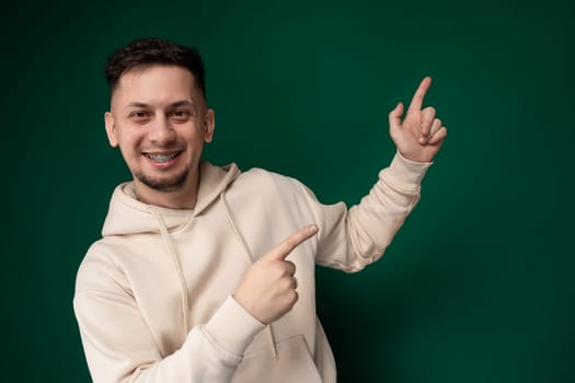 A man wearing a white hoodie is pointing directly at the camera, engaging the viewer with a direct gaze. His gesture is assertive and purposeful, drawing attention to himself.