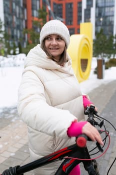 A woman wearing winter clothing is riding a bike down a street covered in snow. The scene captures the activity of cycling in a snowy urban environment.