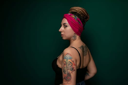 A woman with tattoos on her arms wearing a pink headband. She is standing confidently and looking directly at the camera.