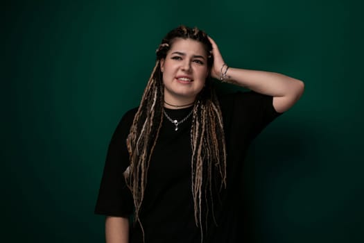 A woman with dreadlocks is standing upright in front of a solid green background. Her hair is styled in long, thin braids, and she is looking directly at the camera.